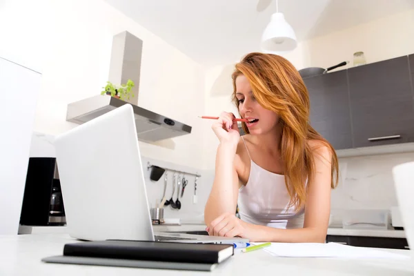 Redhead girl chewing a pencil in kitchen — Stock Photo, Image