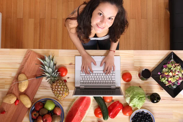 Kvinna som använder en bärbar dator medan matlagning — Stockfoto