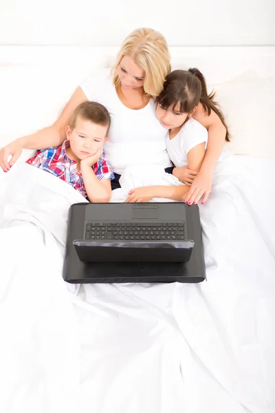 Mama cu copiii ei folosind un laptop în pat — Fotografie, imagine de stoc