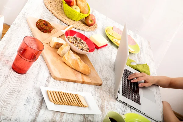 Jeune femme prenant le petit déjeuner tout en utilisant un ordinateur portable — Photo