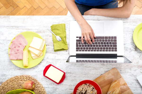 Jonge vrouw ontbijten tijdens het gebruik van een laptopcomputer — Stockfoto