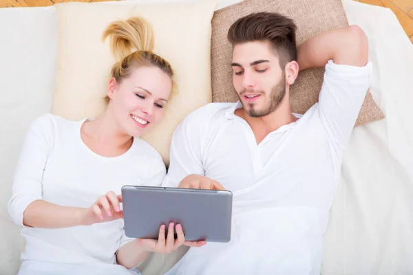 Jeune couple avec une tablette PC au lit — Photo