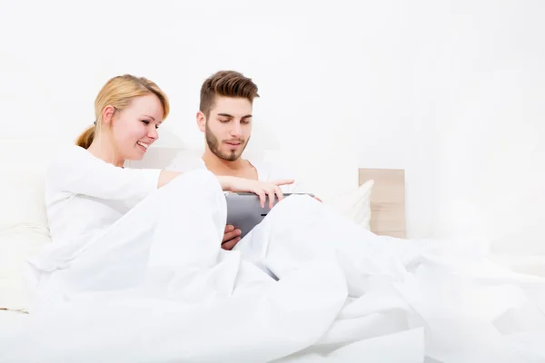 年轻夫妇与一台 tablet pc，躺在床上 — 图库照片
