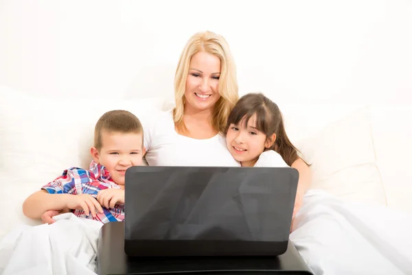 Madre con sus hijos usando un portátil en la cama —  Fotos de Stock