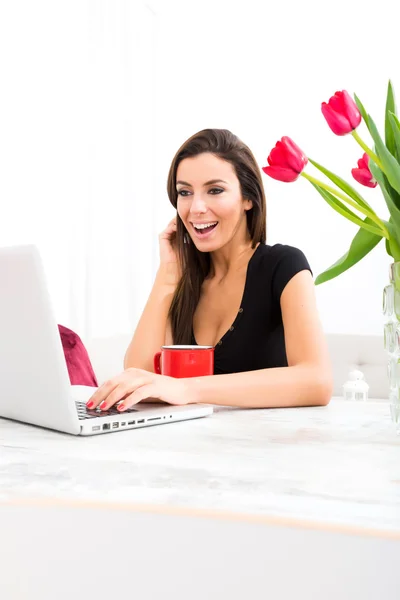 Молода красива жінка посміхається під час використання ноутбука вдома — стокове фото