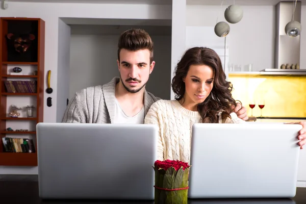 Casal jovem na frente de seus computadores portáteis em casa — Fotografia de Stock