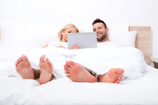 Schönes junges Paar mit einem Tablet-PC im Bett — Stockfoto