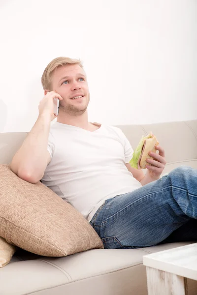 Молодой человек с бутербродом на диване — стоковое фото