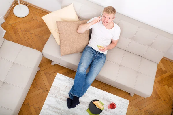 Junger Mann mit Sandwich auf dem Sofa — Stockfoto