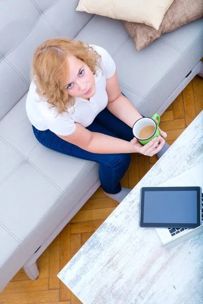 Giovane donna sul divano con gadget — Foto Stock