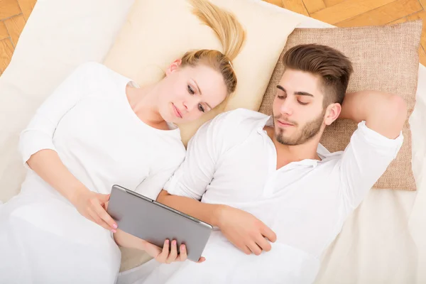 Jeune couple avec une tablette PC au lit — Photo