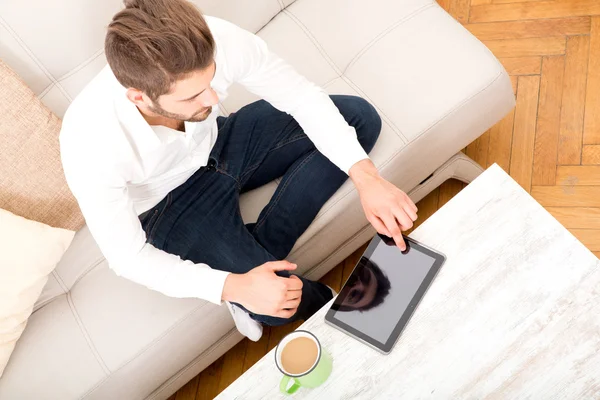 Ung man med tablett på soffan — Stockfoto