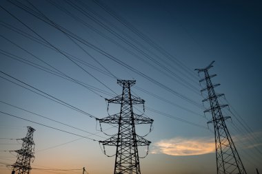 Mavi gökyüzüne karşı elektrik iletim pilonu silueti