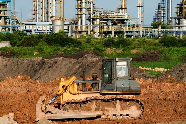 挖掘机在赋值和炼油厂背景 — 图库照片