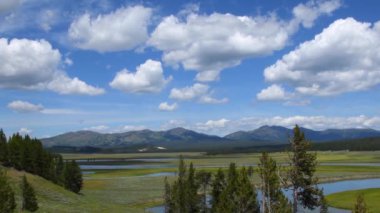 Hayden Vadisi 'nden Yellowstone Ulusal Parkı' ndaki Grand Loop Yolu boyunca uzanan panoramik bir manzara. Sahnede Yellowstone Nehri ve stratocumulus bulutlu mavi gökyüzü yer alıyor. Kamera soldan sağa hareket ediyor.