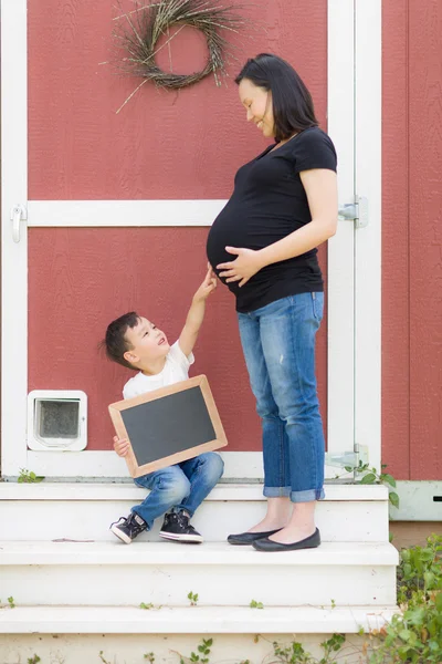 Fils avec tableau blanc de craie pointant vers le ventre enceinte de maman — Photo
