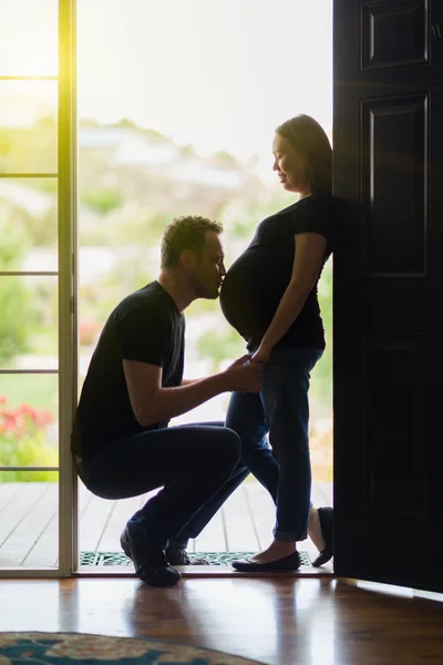 Man kysser magen av gravida hustru i dörröppningen. — Stockfoto