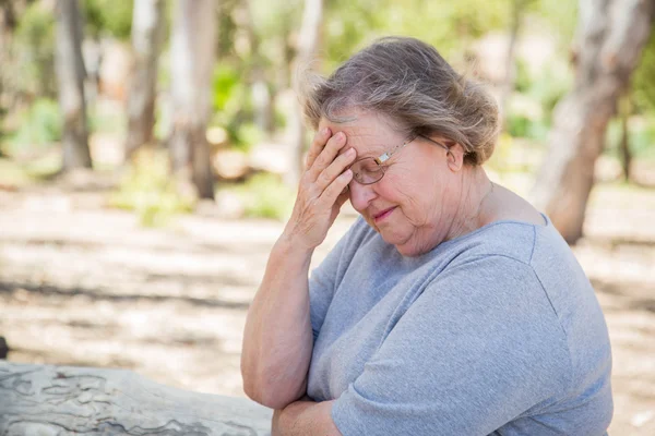 Расстроенная пожилая женщина сидит одна — стоковое фото