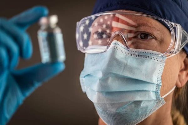 女性医療従事者を反映したアメリカンフラッグ保護顔マスクとゴーグルを装着したワクチンバイアルを保持 — ストック写真