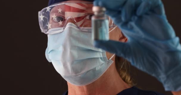 4K医師または看護師が顔マスクを着用し アメリカ国旗反射保持ワクチンバイアルとゴーグル — ストック動画