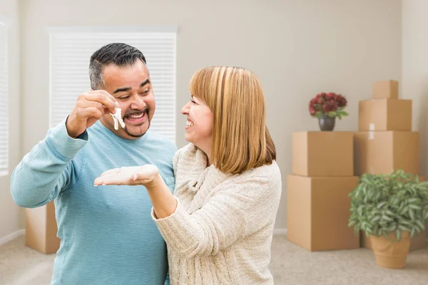 Mixed Race Couple Holding House Keys Inside Empty Room with Moving Boxes.