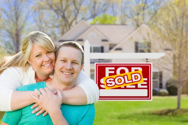 販売不動産の看板と新しい家の前で幸せなカップルの抱擁 ロイヤリティフリーのストック写真