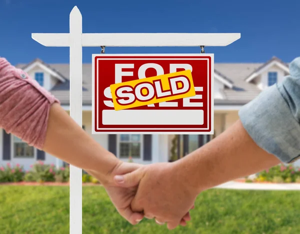 美しい新しい家の前で手を握り 販売のために販売するカップル不動産標識 — ストック写真