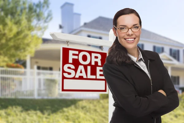 Νεαρή γυναίκα μπροστά από το σπίτι και το σημάδι πώλησης — Φωτογραφία Αρχείου