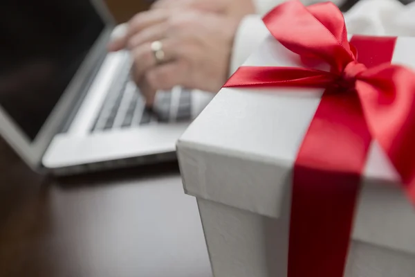 Boîte cadeau blanche avec arc rouge près de l'homme en utilisant un ordinateur portable — Photo