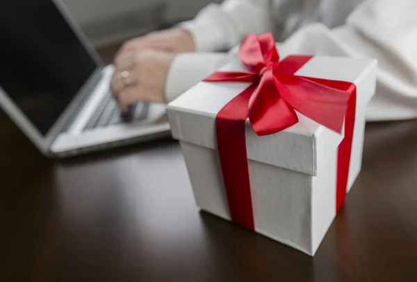 Συσκευασία δώρου λευκό με κόκκινο τόξο κοντά άνθρωπος χρησιμοποιώντας φορητό υπολογιστή — Φωτογραφία Αρχείου