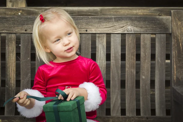 Bedårande liten flicka uppackning hennes gåva på en bänk — Stockfoto