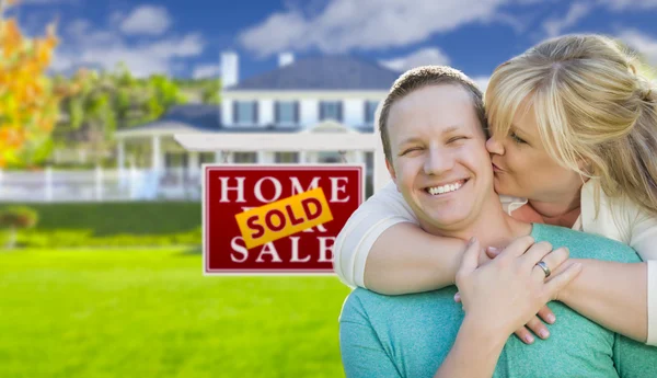 Szczęśliwa para z przodu sprzedawane nieruchomości znaku i domu — Zdjęcie stockowe