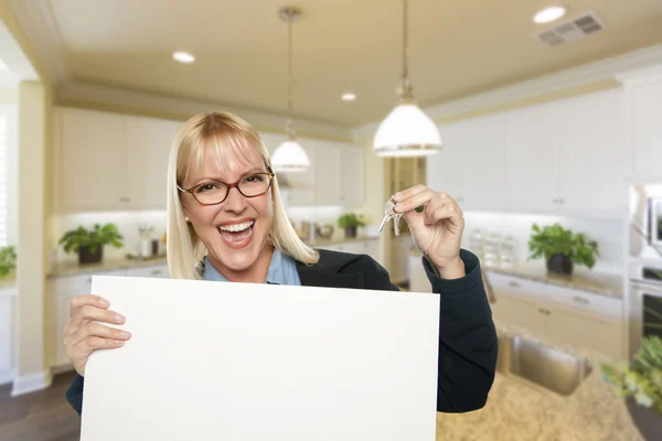 Jonge vrouw met leeg teken en sleutels binnen keuken — Stockfoto