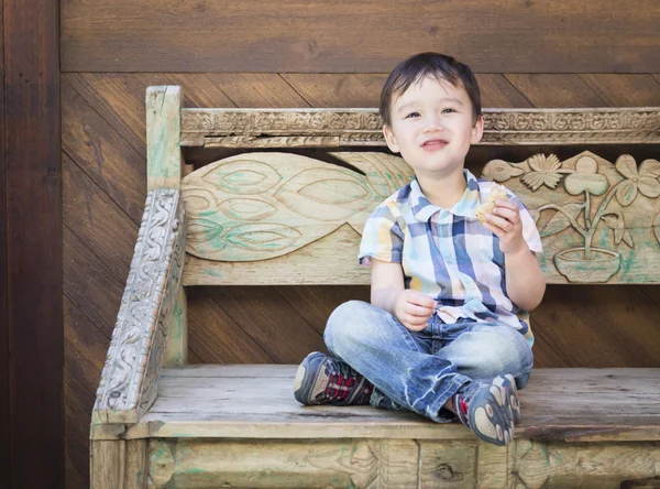 サンドイッチを食べてのベンチに座っているかわいい混血少年 — ストック写真