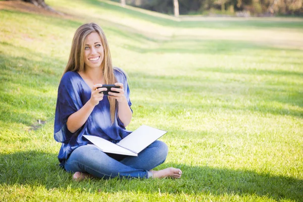 Mujer joven sonriente con libro y teléfono celular al aire libre — Foto de Stock