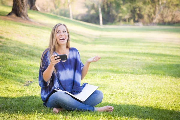 Směje se mladá žena s knihou a mobilní telefon venku — Stock fotografie