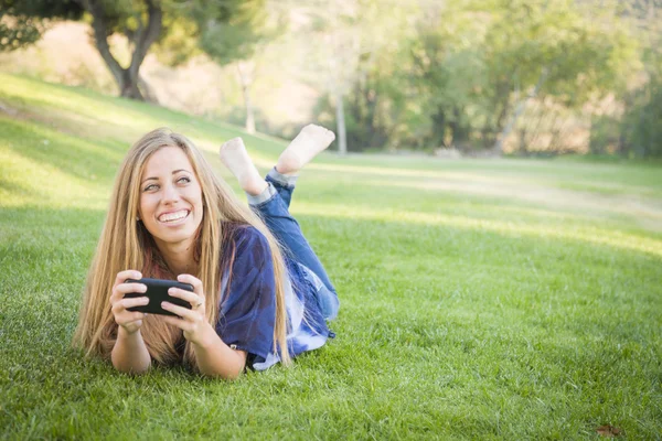 Улыбающаяся молодая женщина использует мобильный телефон на открытом воздухе — стоковое фото