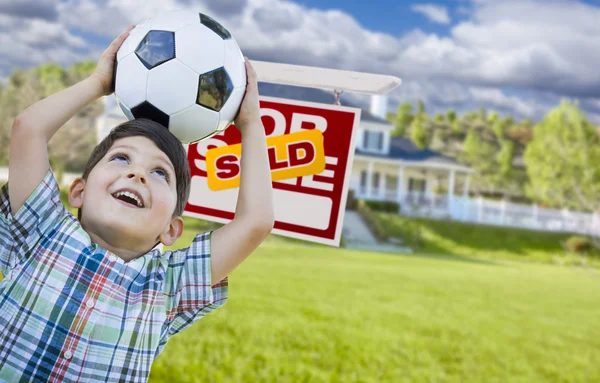 Мальчик держит мяч перед домом и продается знак — стоковое фото