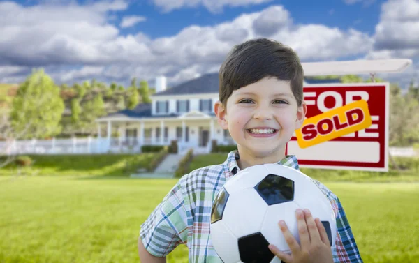 Ev ve satılan işareti önünde topu tutan çocuk — Stok fotoğraf