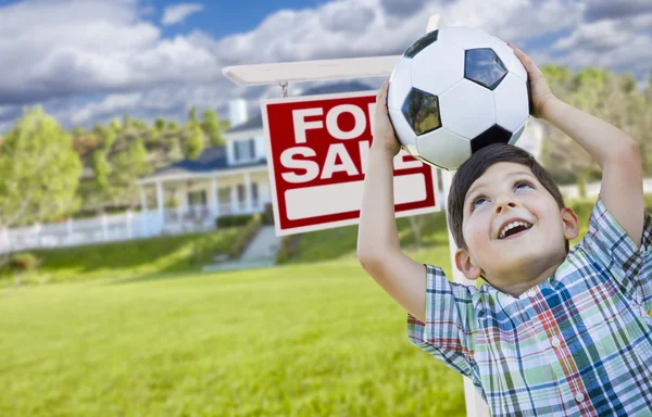 Menino segurando bola na frente da casa e sinal de venda — Fotografia de Stock