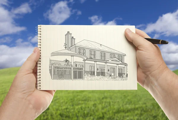Руки держат бумагу с рисунком дома над пустым травяным полем — стоковое фото
