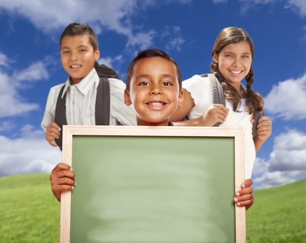 Meninos hispânicos e menina no campo segurando placa de giz em branco — Fotografia de Stock