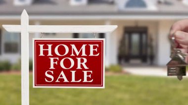 Ajan Hand, yeni evin anahtarını ve anahtarlığını satılık emlak tabelası ve güzel yeni ev tabelasının önünde sunar..