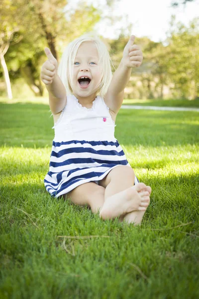 Schattig klein meisje met Thumbs Up in het gras — Stockfoto