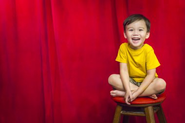 Laughing Boy Sitting on Stool in Front of Curtain clipart