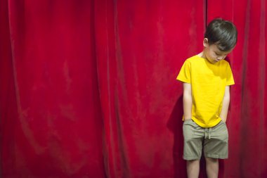 Pouting Mixed Race Boy Standing In Front of Red Curtain clipart