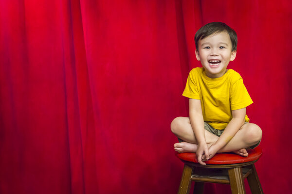 Laughing Boy Sitting on Stool in Front of Curtain