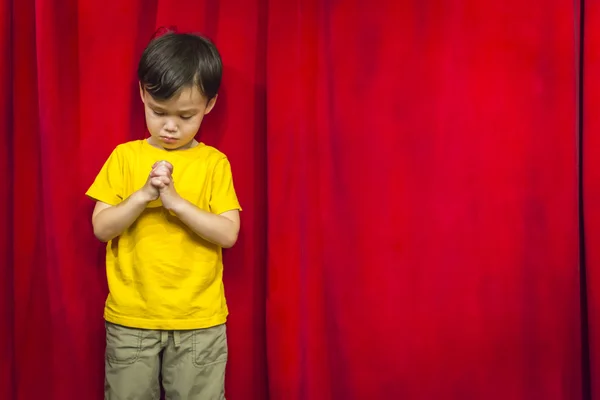 Mixed Race Boy Praying in Front of Red Curtain — Stock Photo, Image