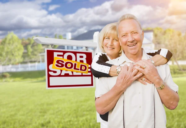 Pareja mayor en frente de la venta de signos de bienes raíces y casa — Foto de Stock