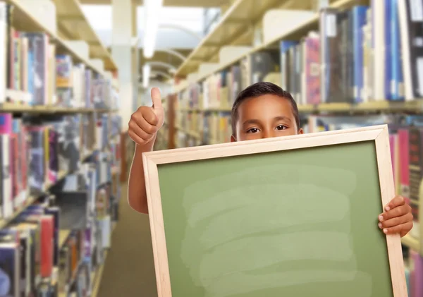 Menino hispânico com placa de giz vazia na biblioteca — Fotografia de Stock